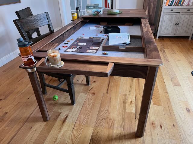 table with most of its toppers removed. A game of Spire's End Hildegard has been laid out. Near the camera you can see a nalgene water bottle and an espresso. Many of the accessories are visible