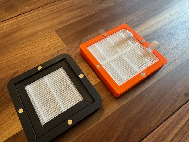 a black plastic square with a hepa filter in it, and an orange plastic square with 2 hepa filters in it.