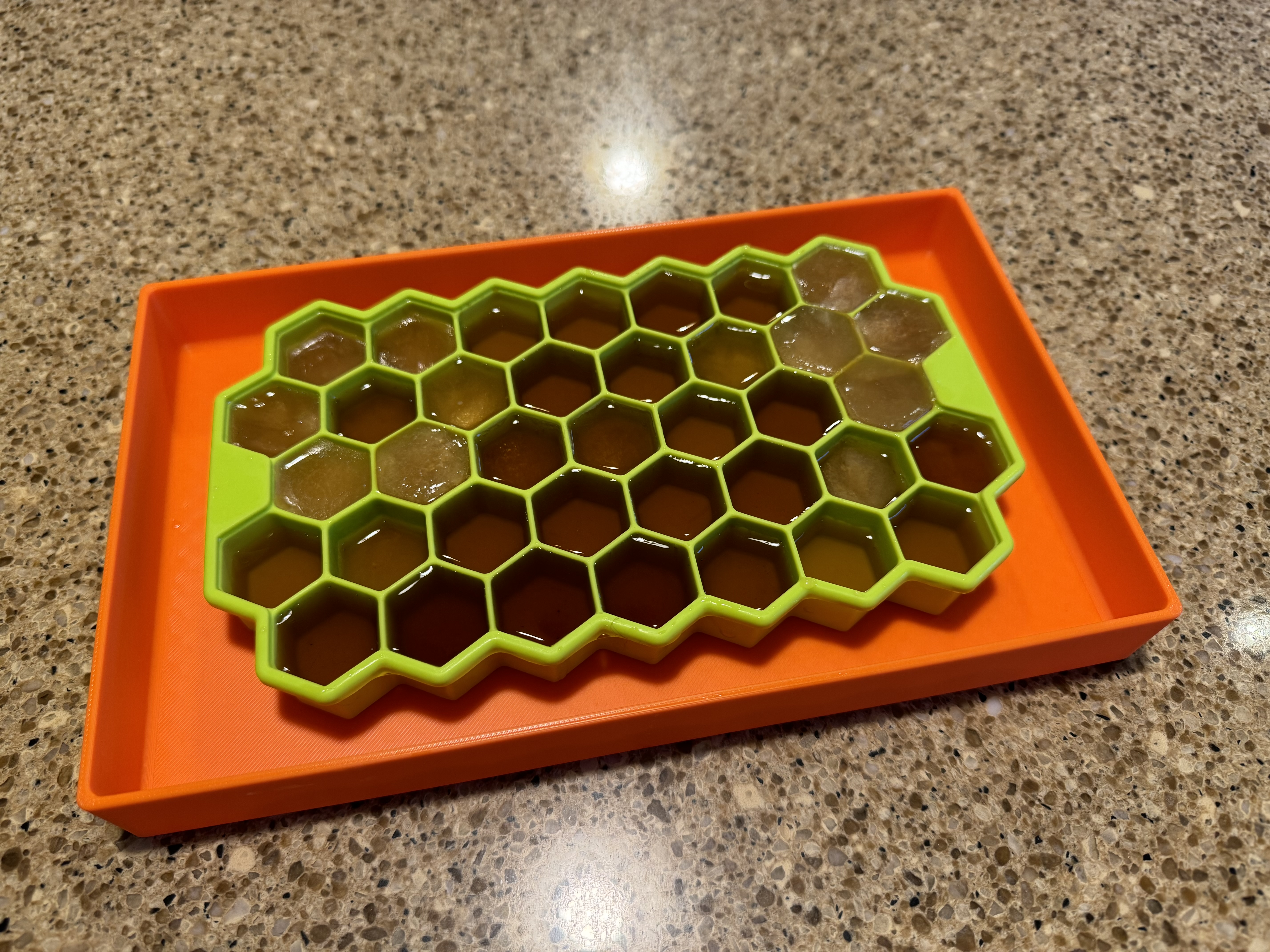 an orange tray with a lime green silicone ice tray that is subdivided into hexagons. within the hexagons is liquid black tea.