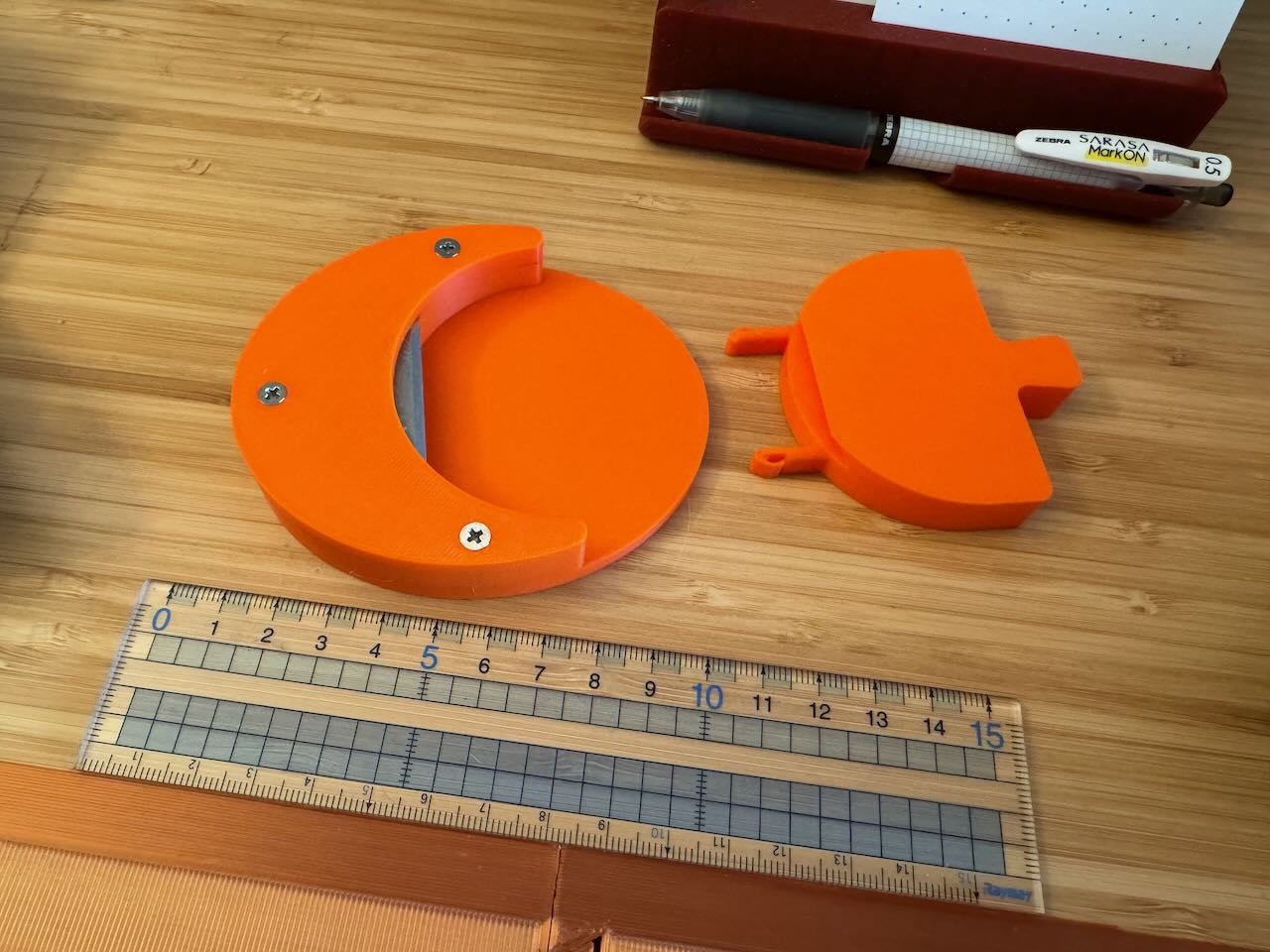 an orange oval with a raised crescent on the left. there are three screws in it that are holding down a piece of plastic that is in turn holding down a rasor blade. to the right is the snap-in blade cover with an easy-pull-tab.