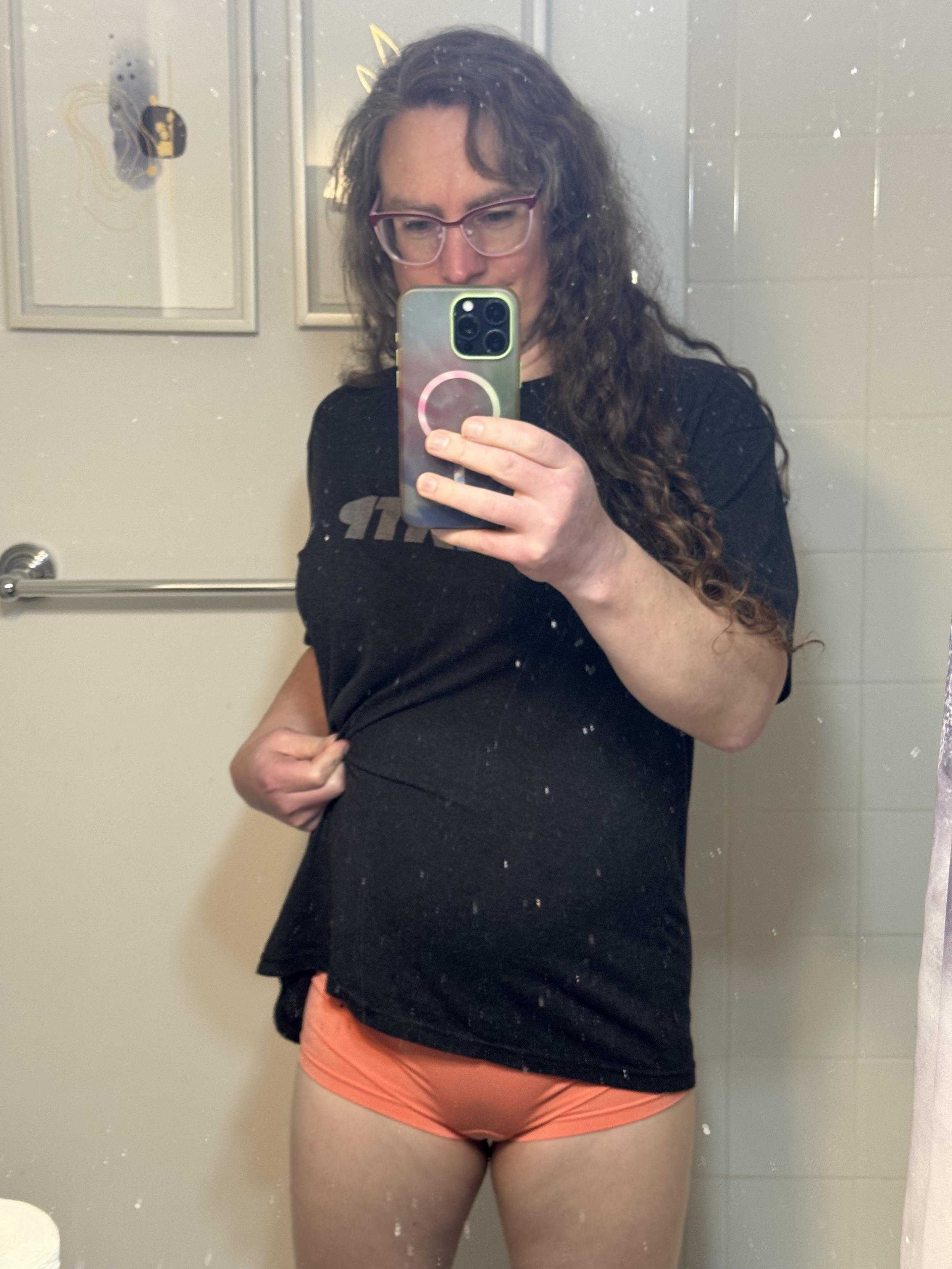 mirror selfie showing me pulling up the bottom edge of my black tshirt to better reveal the salmon colored boy shorts I'm wearing.
